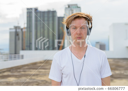 Young handsome man with face shield listening to music at rooftop of the building Young handsome man with face shield listening to music at rooftop of the building 66806777