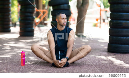 Athletic black guy stretching on asphalt road after his morning workout at park 66809653