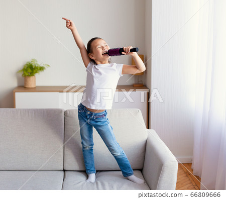 Girl Singing Holding Hairbrush Like Microphone Standing On Sofa Indoor Girl Singing Holding Hairbrush Like Microphone Standing On Sofa Indoor 66809666