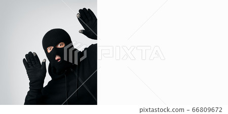 Masked thief with raised arms isolated on white wall Masked thief with raised arms isolated on white wall 66809672