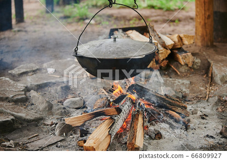 Hiking pot, Bowler in the bonfire. Fish soup boils in cauldron at the stake. Traveling, tourism, picnic cooking, cooking at the stake in a cauldron, fire and smoke. Hiking pot, Bowler in the bonfire. Fish soup boils in cauldron at the stake. Traveling, tourism, picnic cooking, cooking at the stake in a cauldron, fire and smoke. 66809927