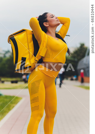 Young woman in yellow shirt delivering food using gadgets to track order at the city's street. Courier using online app for receiving payment and tracking shipping address. Modern technologies. 66810444