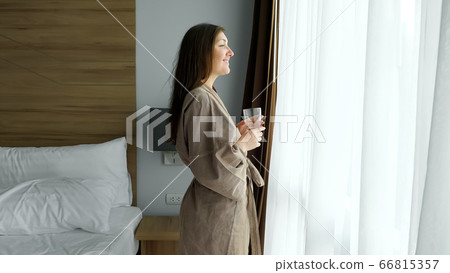 woman drinks clean water standing near window in hotel room woman drinks clean water standing near window in hotel room 66815357