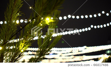 Christmas tree with shiny garland on background of blurry lights of Christmas market and ice rink Christmas tree with shiny garland on background of blurry lights of Christmas market and ice rink 66817486