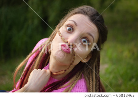 Outdoors female portrait of a modern girl with dreadlocks in pink sweater grimacing like a child in a city park during a sunset, be free, be youself concept 66818462