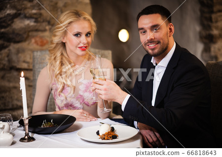 Romance and dating concept. Young couple man and woman with champagne glasses celebrating and toasting in restaurant. Two people male and female in elegant evening suit and dress on romantic dinner Romance and dating concept. Young couple man and woman with champagne glasses celebrating and toasting in restaurant. Two people male and female in elegant evening suit and dress on romantic dinner 66818643