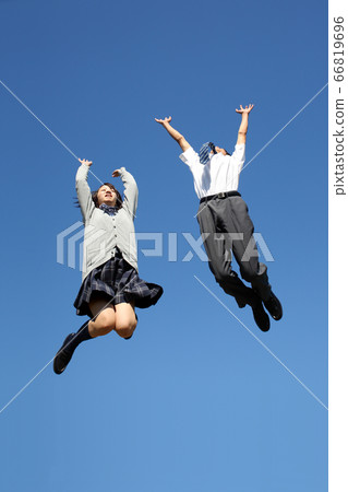 Two male and female high school students jumping while happily against the blue sky. Two male and female high school students jumping while happily against the blue sky. 66819696