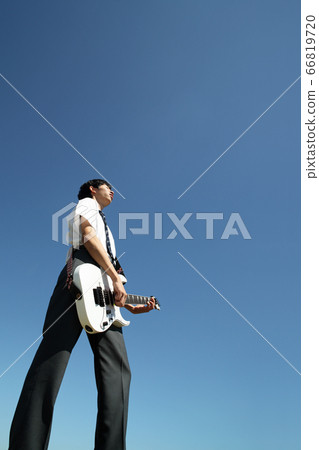 High school boy playing electric guitar outdoors against blue sky 66819720