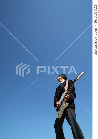 High school boy playing electric guitar outdoors against blue sky 66819722