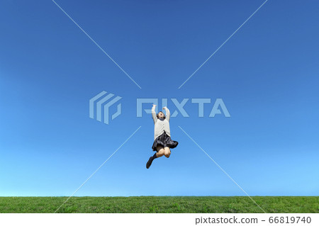 Schoolgirl jumping while playing Banzai against the blue sky 66819740