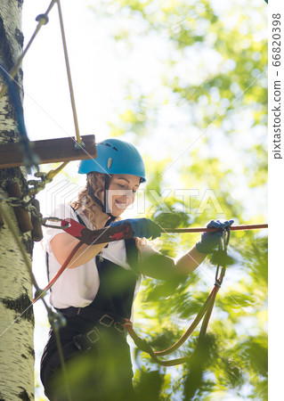 Rope adventure - smiling woman walks on the suspension rope bridge 66820398