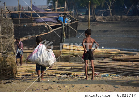 孟加拉國的考克斯·巴扎爾（Cox's Bazar）一個沿海漁村和一條漁船攔住了一個男孩在沙灘上行走以收集資源垃圾 66821717
