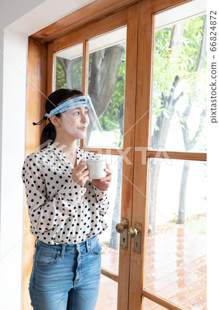Woman wearing a face shield and drinking tea at a cafe Woman wearing a face shield and drinking tea at a cafe 66824872