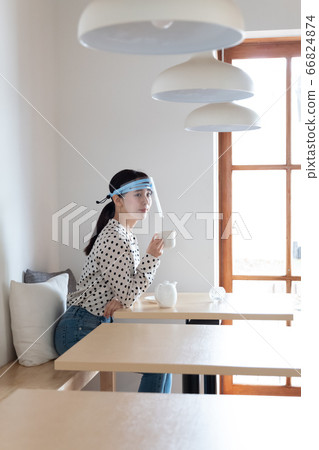 Woman wearing a face shield and drinking tea at a cafe Woman wearing a face shield and drinking tea at a cafe 66824874