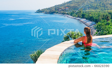 Woman at edge of infinity swimming pool with sea Woman at edge of infinity swimming pool with sea 66828390
