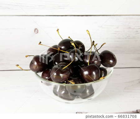 Glass cup with maroon cherries on a light wooden background 66831708