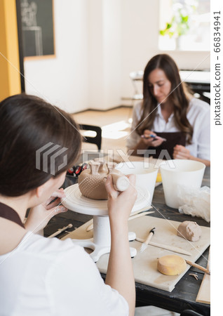Closeup of bottom of mug, which is being decorated in ceramic studio. Female professional hands making clay dots or drops on the surface of vase by special squeezing tool. 66834941