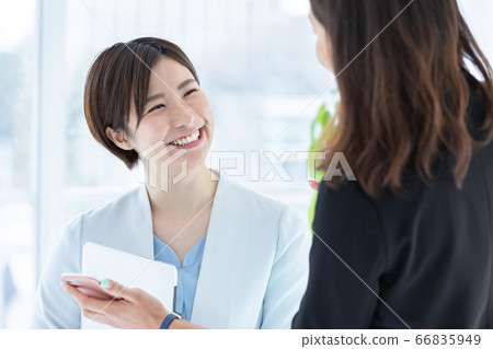 一個年輕的女人,一邊看著商務智能手機交談 一個年輕的女人,一邊看著商務智能手機交談 66835949