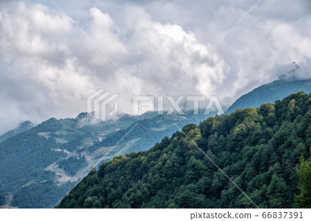 High mountain with green slopes hidden in clouds and fog 66837391