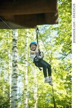 A little girl hanging on the insurance cable of her belt - rope bridge entertainment attraction in the park 66838526