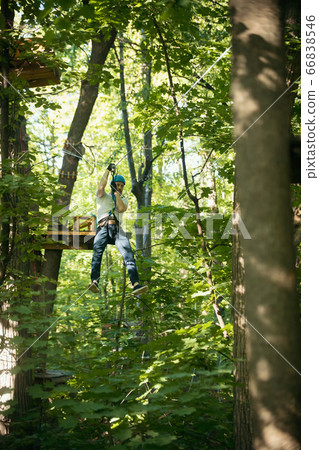 A man having a rope adventure in the forest with full insurance - sliding down using his rope belt A man having a rope adventure in the forest with full insurance - sliding down using his rope belt 66838546