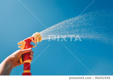 Hand holds yellow hose with nozzle on background of blue sky with water splashes Hand holds yellow hose with nozzle on background of blue sky with water splashes 66842848