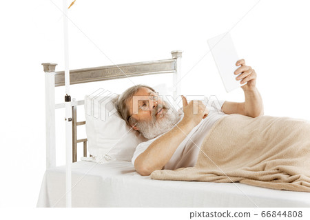Elderly old man recovering in a hospital bed isolated on white Elderly old man recovering in a hospital bed isolated on white 66844808