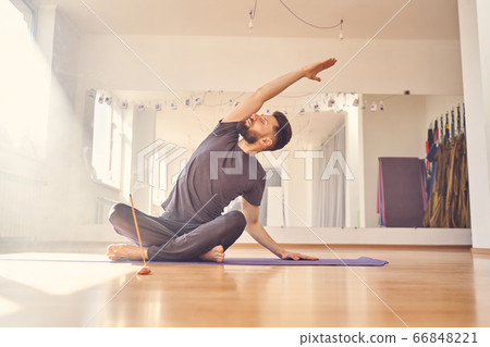 Handsome young man doing stretching exercise in yoga studio 66848221
