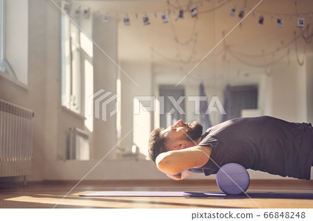 Bearded man lying on foam roller during training in studio 66848248