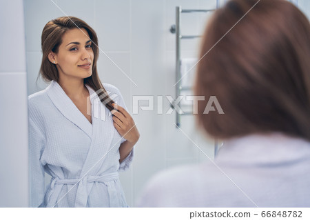 Attractive joyful lady looking in the mirror in bathroom Attractive joyful lady looking in the mirror in bathroom 66848782