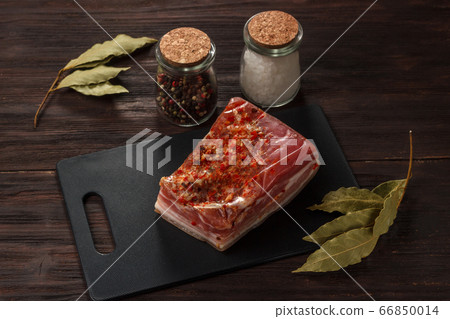 Salty bacon on a board with bay leaf and pepper 66850014