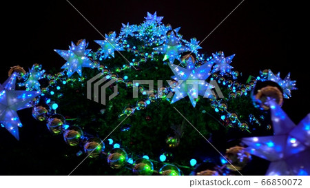 Fantastic whirling around stunning Christmas tree at town square decorated large luminous multi-pointed blue stars and yellow balls 66850072