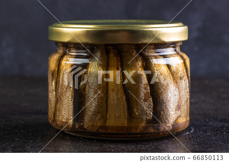 Glass jar of sprats against a dark background 66850113