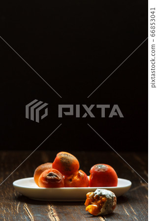 Spoiled rotten apricots on a white saucer on a dark background, vertical with space 66853041
