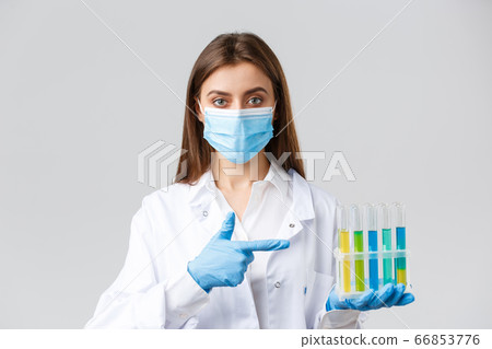 Covid-19, preventing virus, healthcare workers concept. Professional doctor in personal protective equipment, medical mask, pointing at test-tube with coronavirus vaccine, patient samples Covid-19, preventing virus, healthcare workers concept. Professional doctor in personal protective equipment, medical mask, pointing at test-tube with coronavirus vaccine, patient samples 66853776