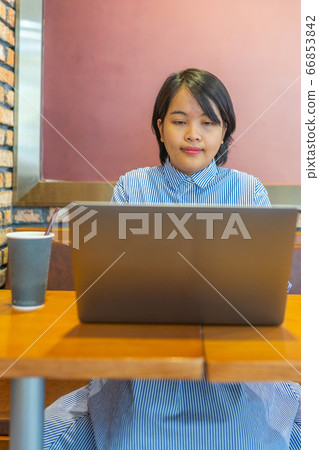 Vertical photo of Asian woman freelancing on laptop at cafeteria Vertical photo of Asian woman freelancing on laptop at cafeteria 66853842