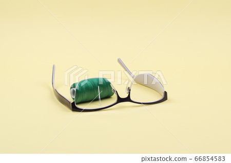 In the inverted glasses see the thread with a needle on a yellow background. In the inverted glasses see the thread with a needle on a yellow background. 66854583