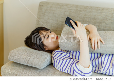 Young woman lying on the sofa and looking at mobile phone Young woman lying on the sofa and looking at mobile phone 66860308