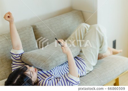 Young woman lying on the sofa and looking at mobile phone Young woman lying on the sofa and looking at mobile phone 66860309