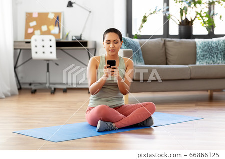 woman with smartphone sits on exercise mat at home 66866125