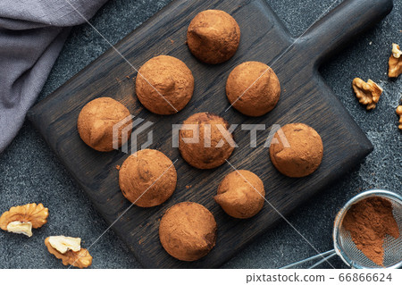 Delicious chocolate truffles sprinkled with cocoa powder and walnuts on a wooden stand. Dark concrete background. 66866624