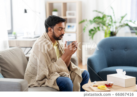 sick young man in blanket drinking hot tea at home 66867416