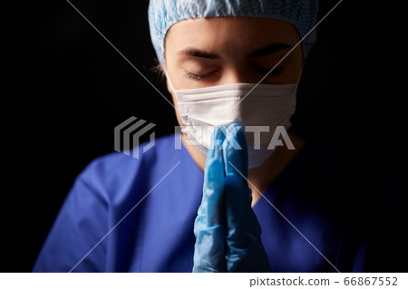 female doctor or nurse in face mask praying 66867552