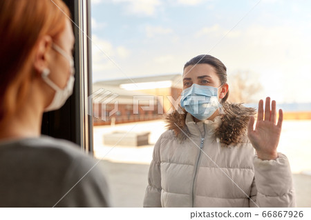 woman in mask looking to friend through window 66867926