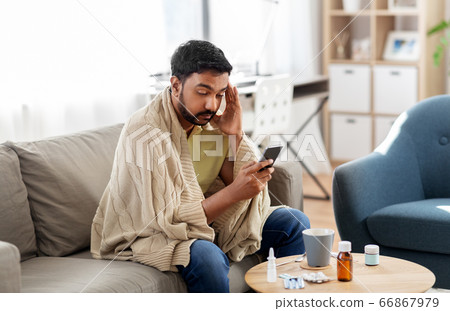 sick young man in blanket with smartphone at home sick young man in blanket with smartphone at home 66867979