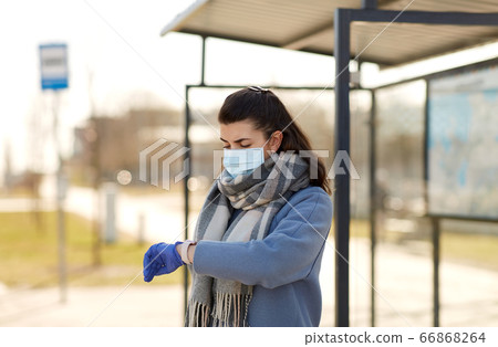 woman in mask looking at wristwatch at bus stop woman in mask looking at wristwatch at bus stop 66868264