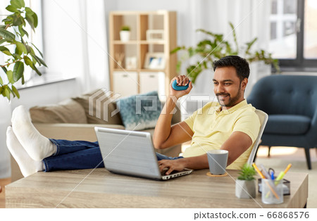 man with laptop and hand expander at home office 66868576