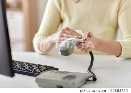 close up of woman cleaning desk phone with tissue 66868753