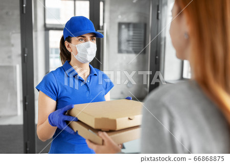 delivery girl in mask giving pizza boxes to woman 66868875