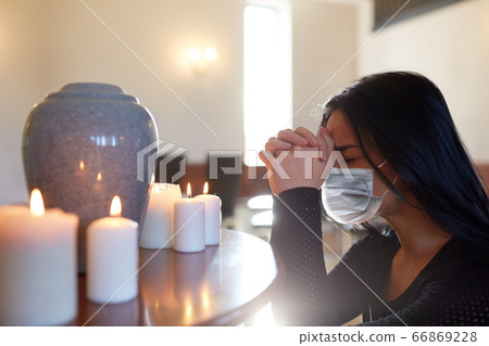 sad woman in mask praying at funeral in church 66869228